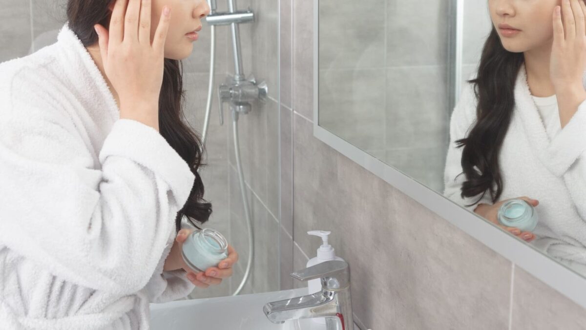 鏡の前で顔にクリームを塗る女性